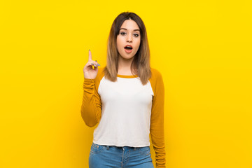 Pretty young woman over isolated yellow wall thinking an idea pointing the finger up