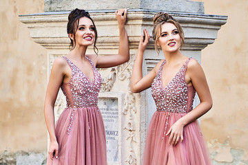 Beautiful bridesmaids in gorgeous elegant stylish red pink violet floor length v neck chiffon gown dress decorated with sequins sparkles and rhinestones standing by an old column. Wedding day in old - obrazy, fototapety, plakaty