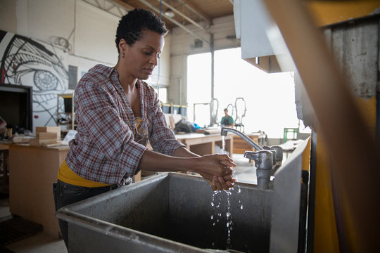 Mature woman washing hands in sink in workshop