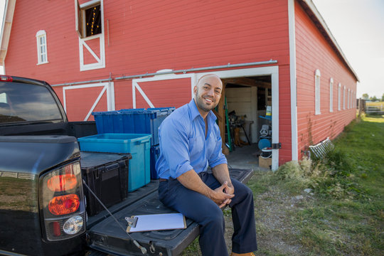 Portrait smiling event delivery man sitting at truck bed outside barn