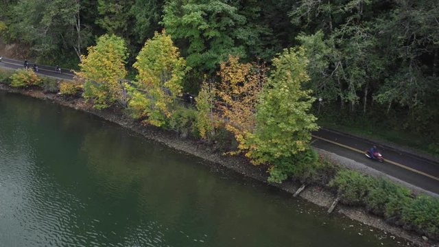 Aerial view of motorcycles riding together past fall trees on a road next to water in Washington