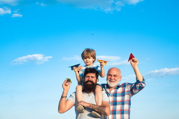 Happy grandfather father and grandson with toy paper airplane over blue sky and clouds background. Happy men loving family. Father son and grandfather relaxing together.