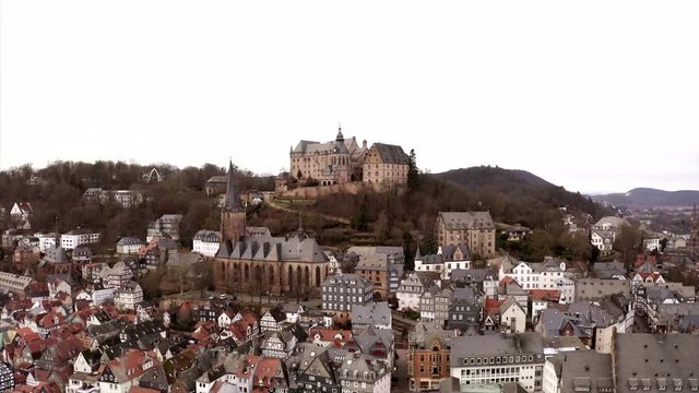 The cityscape of Marburg in Hesse, Germany in a drone pan across the roofs of the town with its university.