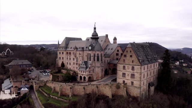 Establishing shot filmed by drone in Marburg, Germany. The camera flies slowly backwards from the castle over the cityscape of the town famous for its university.