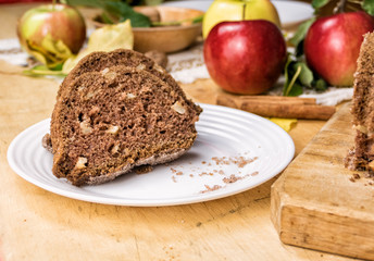 Obraz na płótnie Canvas Sliced apple cinnamon bread with decorations on wooden table. Made from apples, sugar, oil, eggs, flour. Homemade apple loaf cake on plate with fresh apples and cinnamon in background at autumn