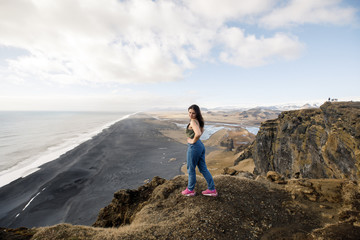 Fototapeta premium młoda podróżniczka w pobliżu klifu z widokiem na czarną plażę i Ocean Atlantycki na Islandii