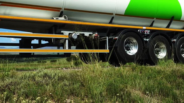 Large petrol gasoline tanker truck driving past with Maloti mountain range and farms in Free-state province near Camelroc town and the Lesotho border. Roadside grass and flowers moving in the wind.