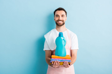 happy bearded man holding clean clothes and laundry detergent on blue