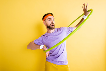 confused sportsman exercising with hula hoop on yellow