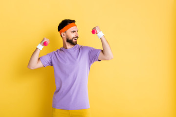 happy bearded sportsman holding small dumbbells while working out on yellow