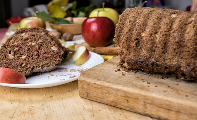 Sliced apple cinnamon bread with decorations on wooden table. Made from apples, sugar, oil, eggs, flour. Homemade apple loaf cake on plate with fresh apples and cinnamon in background at autumn