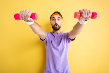 selective focus of bearded sportsman exercising with small pink dumbbells on yellow