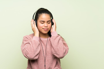 Young teenager Asian girl over isolated green background listening to music with headphones