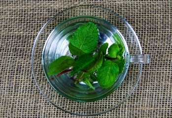Top view on isolated transparent tea glass cup with fresh mint leaves. jute mat background.