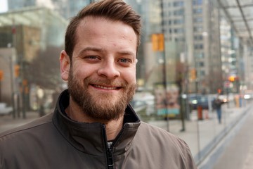 Man with a beard smiling in downtown Toronto with sky rise buildings in the background