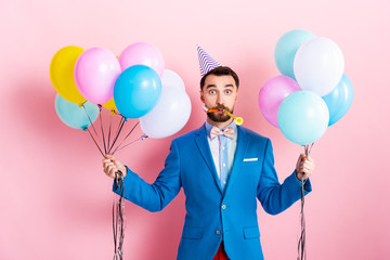 businessman in party cap holding balloons on pink