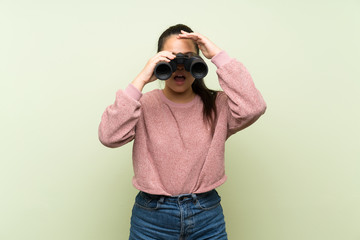 Young teenager Asian girl over isolated green background with black binoculars