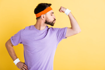 side view of sportsman sending air kiss to muscle isolated on yellow