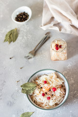 Fermented cabbage with cranberry in ceramic bowl over light grey stone background. Homemade sauerkraut with cranberry and black pepper. Probiotics food concept. Preserved vegetarian diet. 