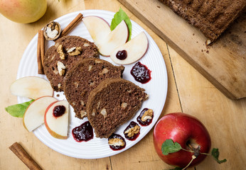 Sliced apple cinnamon bread with decorations on wooden table. Made from apples, sugar, oil, eggs, flour. Homemade apple loaf cake on plate with fresh apples and cinnamon in background at autumn