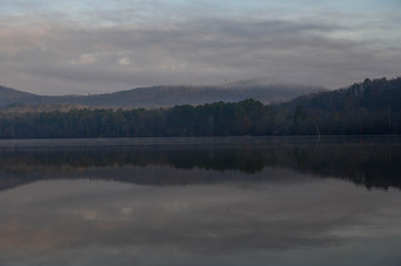 The reflections of the rolling mountains on a cloudy early morning. The haze over the water on a cold winter sunrise morning.