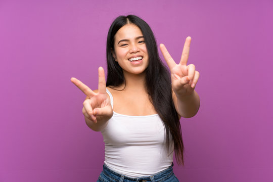 Young teenager Asian girl over isolated purple background smiling and showing victory sign