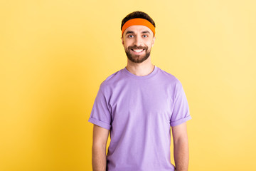 cheerful sportsman in headband smiling isolated on yellow