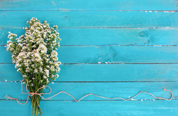 A bouquet of white cutter flower tied with rope on light blue wooden background. Flowers composition. Flat lay. Copy space on blackboard.