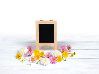 Little chalkboard sign with wooden frame and many flowers on white wooden background. Wedding Decoration. Flowers composition. Flat lay. Copy space on chalkboard sign.