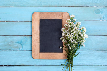 A bouquet of white cutter flower with blackboard on light blue wooden background. Flowers composition. Flat lay. Copy space on blackboard.