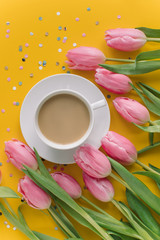 Cup of coffee with milk, bright tulips, confetti on yellow background. Birthday card concept.