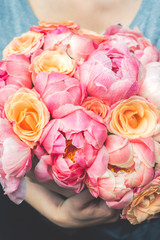 Womans hands are holding fresh bunch of pink peonies and roses. Toned image, card concept, pastel colors
