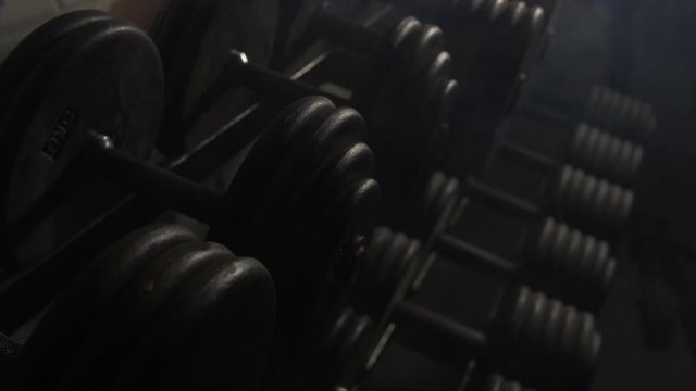 Close Up Pan Across Of Weights Lined Up On Weight Rack In Industrial Gym Old Style Old Fashioned Under Ground Gym. Paint Work Scratched Off Smoke Passing Over Dark Dim Room