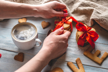 Cup of coffee and hands tying a bow on a gift box with a red ribbon. Romantic Valentine's day gift
