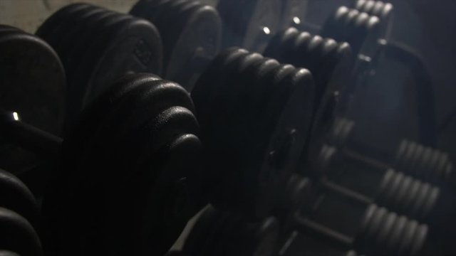 Close Up Pan Across Of Weights Lined Up On Weight Rack In Industrial Gym Old Style Old Fashioned Under Ground Gym. Paint Work Scratched Off Smoke Passing Over Dark Room