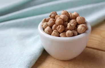 Side on view of a white bowl filled with chick peas (Cicer arietinum), on a wooden table with mint green table cloth. With copyspace.
