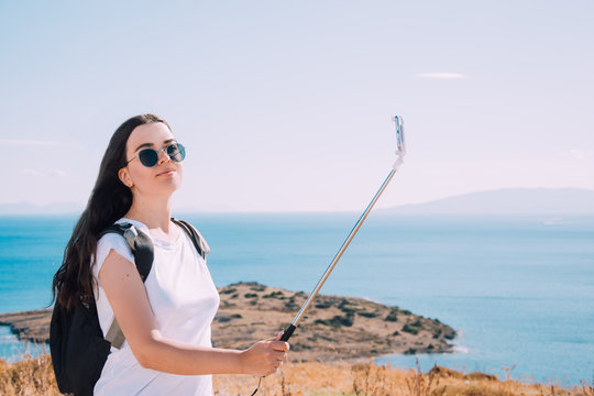 Girl makes selfie on the background of the sea.Traveling in Turkey, Bodrum.Blogger traveler takes photo.Girl in white T-shirt on vacation. Young brunette takes photo on the phone.Selfie on smartphone.