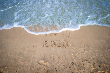 2019 in Sand geschrieben wird überspült von Welle, in Sand geschriebene 2020 im vordergrund