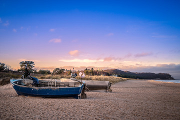 Fototapeta premium 2 Fischerboote am Strand mit Steilküste im Hintergrund vor beginnendem Abendrot