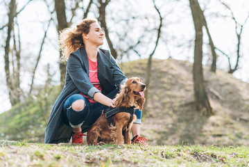 Attractive young curly woman with her brown cocker spaniel posing in the park