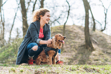 Attractive young happy curly woman with her brown cocker spaniel posing in the park