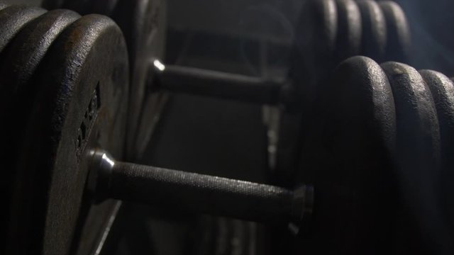 Close Up Pan Over The Top Of Weights Lined Up On Weight Rack In Industrial Gym Old Style Old Fashioned Under Ground Gym. Paint Work Scratched Off Smoke Passing Over