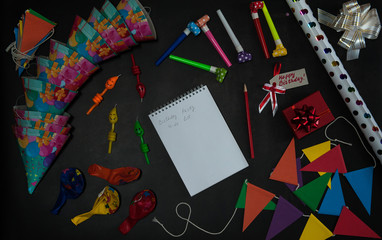 The concept of birthday. Preparing for the party. Notepad, pencil, to-do list, accessories and paper decorations for the holiday on a black concrete background.