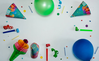 The concept of birthday. The frame is made of paper decorations, confetti and serpentine, cone-shaped caps, blowouts, cake candles and balloons on a light gray background.