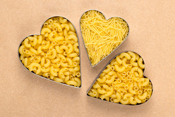 Uncooked pasta on brown paper. Raw macaroni in the shape of a heart. A heap of yellow noodles.