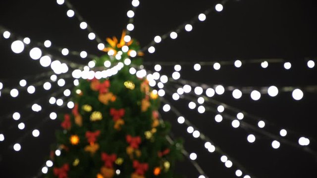 View from the bottom on the beautiful Christmas tree with colorful decorations and garland of white lights standing on the square. Concept. Beautiful snowy winter scenery of Christmas holiday