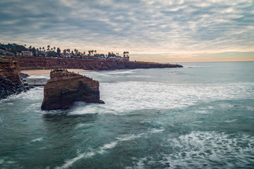 Long exposure surf crashing against beach bluffs on a cloudy day