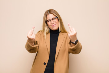 young blonde woman feeling provocative, aggressive and obscene, flipping the middle finger, with a...