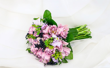 Ramo de peonías de color morado con arándanos y hojas verdes sobre el vestido de una novia