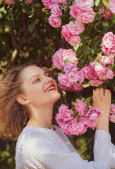 Fototapeta premium Pink rosebush blooming. Happy woman walking at rose garden. Relaxing and happiness concept. Young smiling girl enjoys pink rose flowers. Flowers of pink rose.